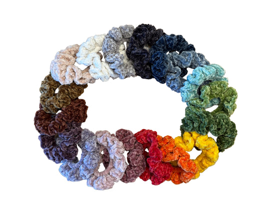 Assorted colorful crocheted scrunchies arranged in a circular pattern on a white background.