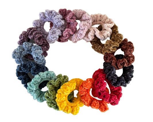 Assorted colorful crocheted scrunchies arranged in a circular pattern on a light background.