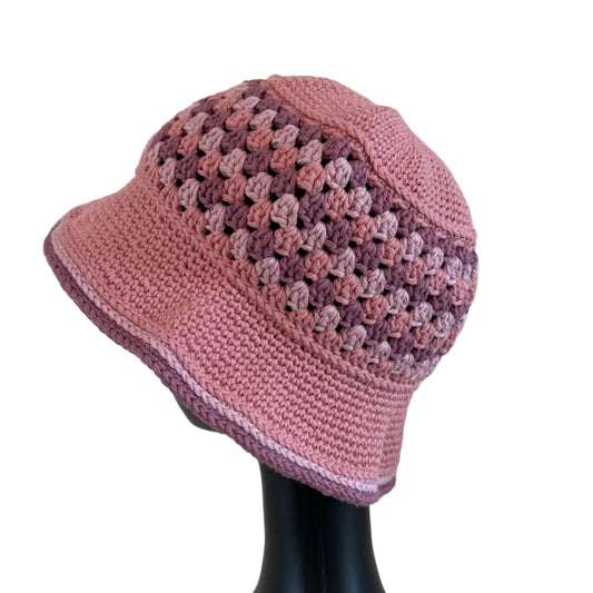 A mauve-rose crocheted bucket hat displayed on a black mannequin head on a white background