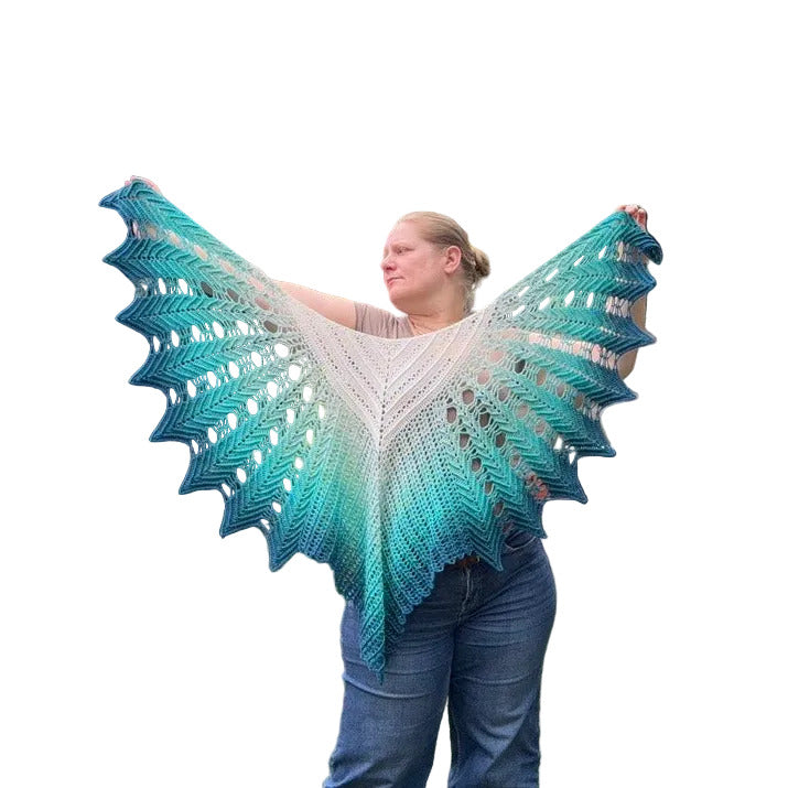 A woman wearing a large, open-front, scalloped crochet shawl with a teal and aqua gradient, held wide out against a plain white background.